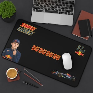 May include: Black rectangular desk mat featuring a Formula 1 theme. The mat has the text "SIMPLY LOVELY" and "DU DU DU DU". It also features a cartoon image of a driver and a race car. A computer mouse is on the mat.