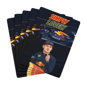 May include: A set of black playing cards featuring a Formula 1 race car and a portrait of a driver. The cards have the words "SIMPLY LOVELY" in yellow and blue. The driver is wearing a blue cap and uniform.