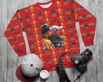 May include: Red crewneck sweatshirt with a repeating pattern of Christmas trees, the Red Bull logo, and the words "Simply Lover" and "Merry Christmas." The sweatshirt features a graphic of two people wearing hats and sunglasses.