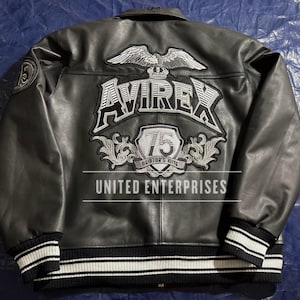 May include: Black leather jacket with white and black striped cuffs and collar. The back features a large embroidered design with the word "AVIREX", an eagle, and the text "75 Aviator's King". The text "UNITED ENTERPRISES" is also visible.