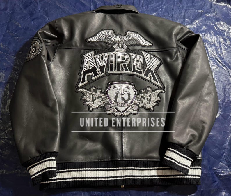 May include: Black leather jacket with white and black striped cuffs and collar. The back features a large embroidered design with the word "AVIREX", an eagle, and the text "75 Aviator's King". The text "UNITED ENTERPRISES" is also visible.