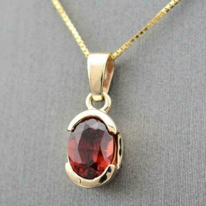 Puede incluir: Un collar con colgante de oro con una piedra preciosa ovalada de color rojo intenso. La piedra preciosa está engastada en un bisel de oro, y el collar tiene una fina cadena de oro. El colgante es un diseño clásico, adecuado para el uso diario o ocasiones especiales.