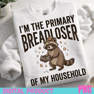 Op de afbeelding: Witte sweatshirt met de tekst "I'M THE PRIMARY BREADLOSER OF MY HOUSEHOLD" in donkerbruin. Een cartoon wasbeer met een hoed en een boek is afgebeeld onder de tekst. De woorden "DIGITAL PRODUCT" en "PNG" staan onderaan.