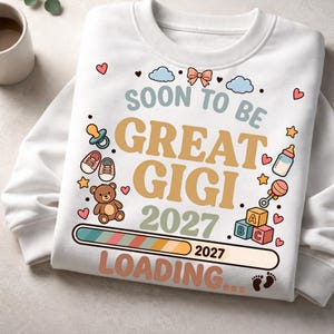 May include: A white crewneck sweatshirt featuring the text SOON TO BE GREAT GIGI 2027 LOADING... along with a loading bar graphic. The design includes illustrations of a teddy bear, baby shoes, a pacifier, a baby bottle, a rattle, and ABC blocks.