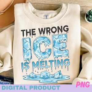 Puede incluir: Sudadera color crema con el texto "THE WRONG ICE IS MELTING" en negro y azul. La palabra "ICE" está diseñada para parecer cubitos de hielo derritiéndose. Debajo del texto hay tres cubitos de hielo derritiéndose en un charco.