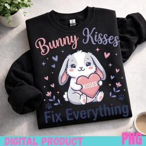 Könnte beinhalten: Schwarzes Sweatshirt mit einer Grafik eines Cartoon-Hasen, der ein rosa Herz mit der Aufschrift "Kisses" hält. Der Text "Bunny Kisses Fix Everything" befindet sich über und unter dem Hasen. Rosa und lila Herzen und Sterne verzieren das Design. Die Wörter "DIGITAL PRODUCT" und "PNG" stehen unten.