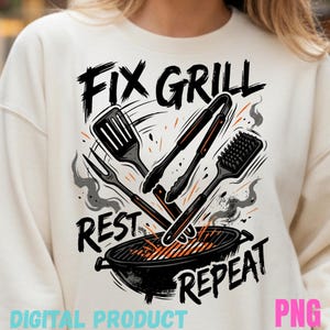 Könnte beinhalten: Cremefarbenes Sweatshirt mit einem grafischen Design, das Grillwerkzeuge und einen Grill zeigt. Der Text lautet "Fix Grill, Rest, Repeat". Das Design umfasst einen Pfannenwender, eine Zange, eine Gabel und eine Grillbürste. Die Wörter "Digital Product" und "PNG" sind ebenfalls sichtbar.