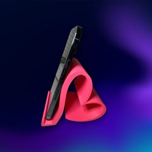 May include: A black smartphone is propped up on a bright pink, heart-shaped phone stand. The stand is made of a flexible material and has a curved design. The background is a gradient of dark blue and purple.