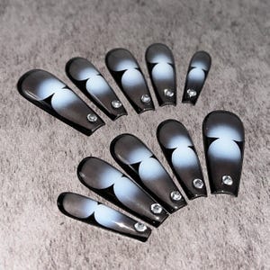 May include: Set of artificial nails in a coffin shape. Each nail features a gradient design of black, gray, and white, with a heart-shaped accent. A small, clear rhinestone is placed at the base of each nail.