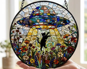 May include: A circular stained glass suncatcher featuring a black cat reaching towards a blue and metallic-toned UFO hovering above a vibrant garden filled with multicoloured flowers, all enclosed within a thin black metal frame with a hanging chain.