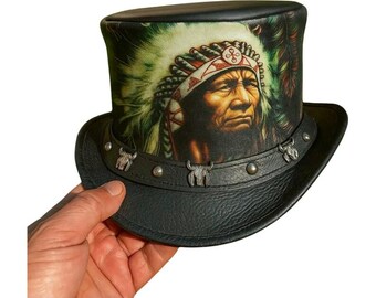 Puede incluir: Sombrero de copa de cuero negro con un retrato de un jefe nativo americano. El sombrero tiene un ala ancha y está adornado con detalles de cabeza de toro plateados y tachuelas alrededor de la base. La copa del sombrero muestra una imagen detallada del jefe.