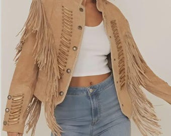 May include: Tan suede jacket with fringe detailing on the sleeves and chest. The jacket features a button-up front and decorative stitching. A stylish outerwear piece.