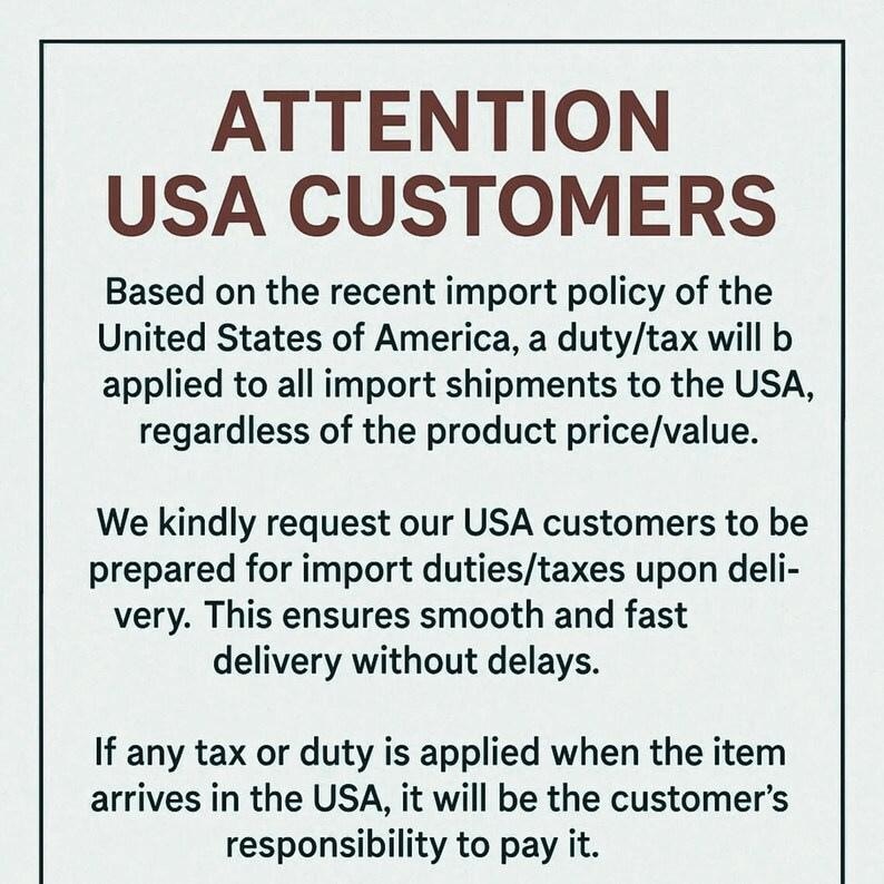 Op de afbeelding: Een witte achtergrond met bruine tekst. De tekst luidt "ATTENTION USA CUSTOMERS", gevolgd door informatie over invoerrechten en belastingen voor zendingen naar de VS. De tekst adviseert klanten zich voor te bereiden.