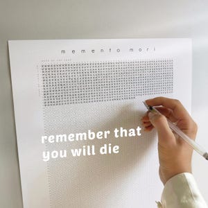 Pu&ograve; includere: Stampa su carta bianca con le parole "memento mori" e "remember that you will die". La stampa ha un motivo a griglia e viene contrassegnata con una penna. La stampa &egrave; un promemoria della mortalit&agrave;.