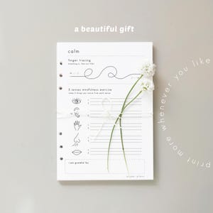 May include: A white planner with mindfulness exercises, tied with white string and adorned with white flowers. The planner includes prompts for finger tracing and a 5 senses exercise. Text reads "a beautiful gift" and "print more whenever you like."