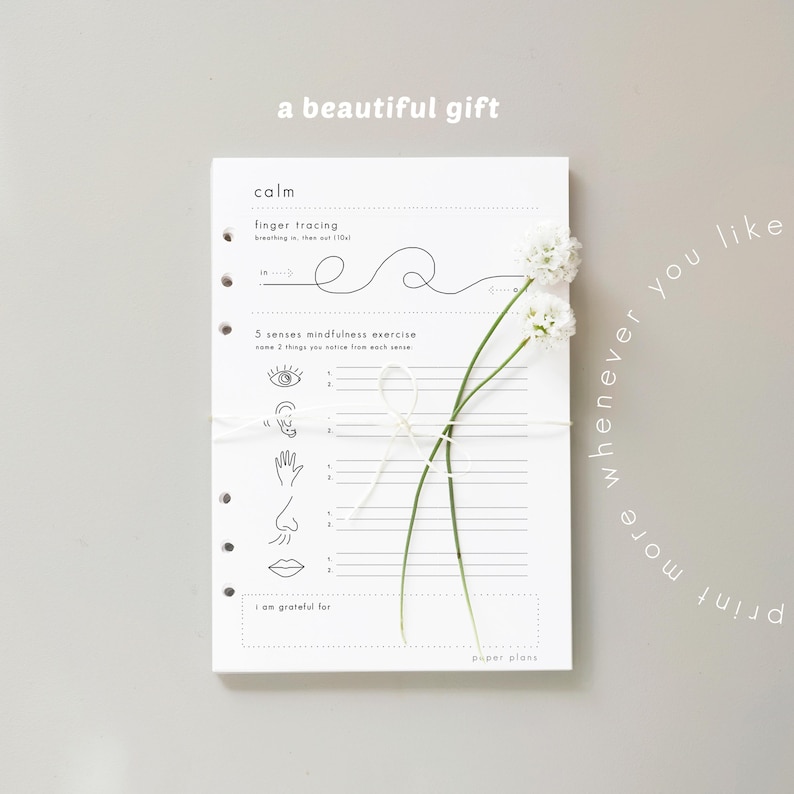 May include: A white planner with mindfulness exercises, tied with white string and adorned with white flowers. The planner includes prompts for finger tracing and a 5 senses exercise. Text reads "a beautiful gift" and "print more whenever you like."