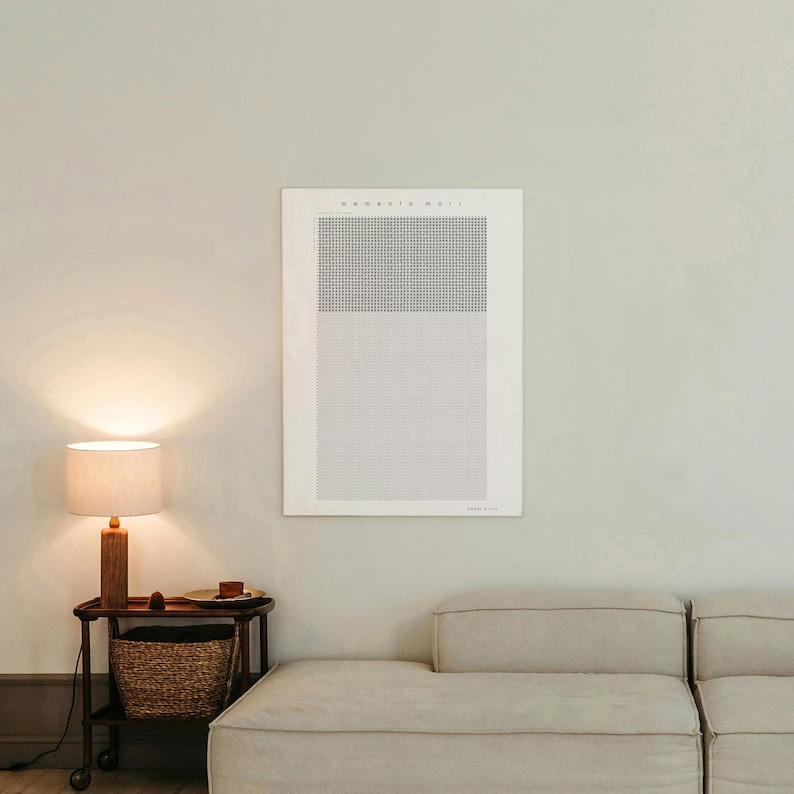 Pu&ograve; includere: Una stampa incorniciata con il testo "Memento Mori" in stile minimalista. L'opera presenta un motivo a griglia in bianco e nero. Una lampada in legno con paralume beige &egrave; su un tavolino con un cestino intrecciato.