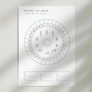 May include: A white paper print with the text "monthly sun salute" and a circular diagram illustrating yoga poses. The diagram is divided into sections numbered 1-31, with the months of the year listed above. The bottom has a key section and the words "paper plans".