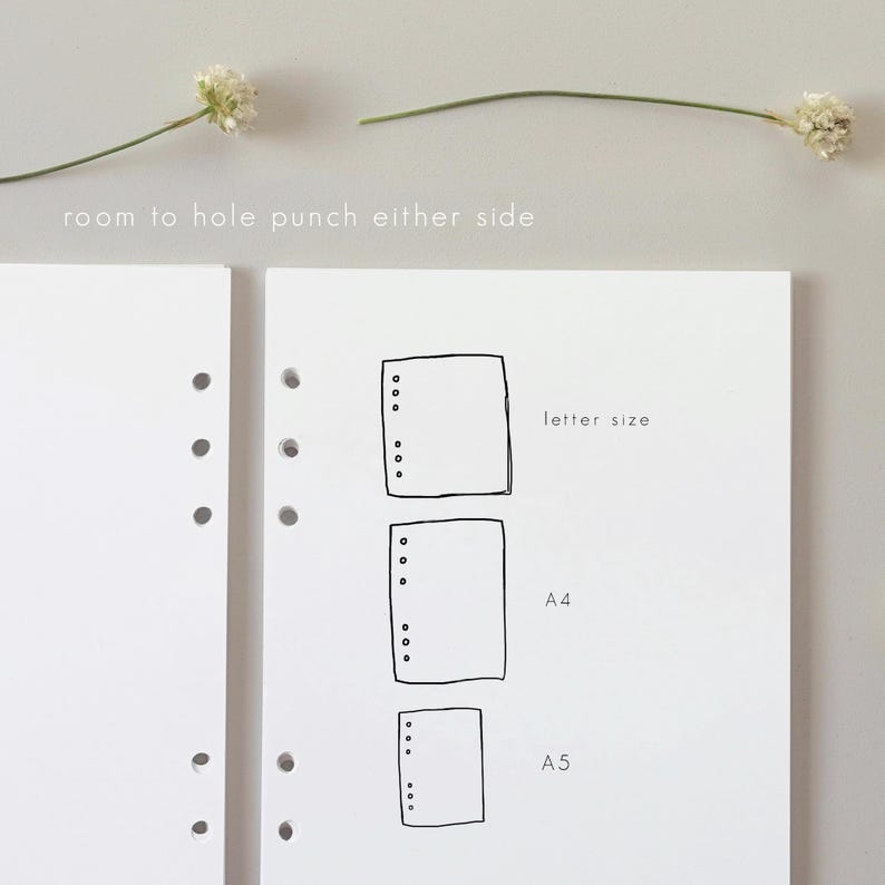 May include: White paper with a sketched design of three different sized rectangles, labeled "letter size", "A4", and "A5". The text "room to hole punch either side" is above the paper. Two sprigs of white flowers are on the top.