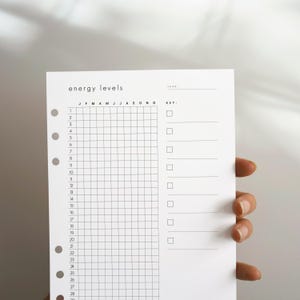 May include: A white planner insert page with black text and grid lines. The header reads energy levels and year. A grid tracks months J through D and days 1 through 31. A key section on the right features empty checkboxes with lines for notes.