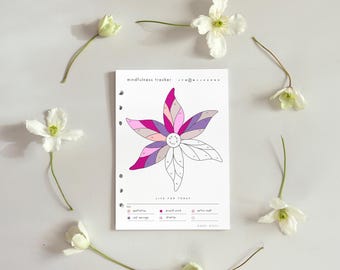 May include: A white planner page with a flower design in shades of pink, purple, and gray, surrounded by white flowers. The text "mindfulness tracker" and "LIVE FOR TODAY" are visible. The planner has a ring binder hole punch.