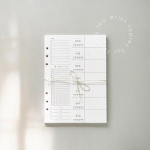 May include: A white weekly planner with sections for each day, a to-do list, and a habit tracker. The planner is bound with string and includes the text "too. print copies for f ends."