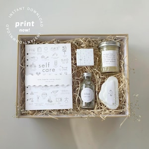 May include: A self-care gift box with a journal, bath salts, a jar of green powder, and a soap dish. The journal has the words "self care" and illustrations. The box is filled with straw and has the words "print now!" in the top left corner.