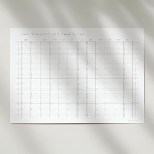 May include: A white wall calendar for the year two thousand and twenty six with black text and grid lines. The calendar displays all twelve months from January to December in a vertical layout with dates one through thirty one listed clearly.