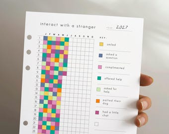 May include: A white paper planner insert titled interact with a stranger for the year 2027. It features a grid with numbered rows and monthly columns, partially filled with coloured squares. A key defines colours for smiled, asked a question, complimented, offered help, asked for help, patted their dog, and had a little chat.