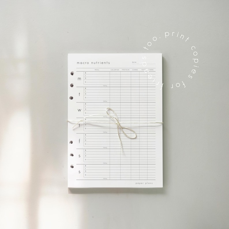 May include: A white paper planner with the words "macro nutrients" at the top. The planner is bound with a string and has columns for meal, calories, protein, carbs, and fat. The days of the week are listed down the side.