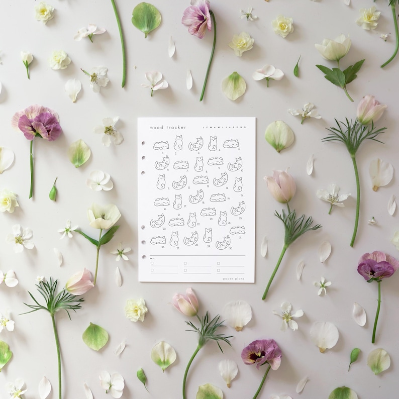 May include: A white mood tracker planner page with cat illustrations, surrounded by scattered flowers and petals in shades of pink, white, and green. The planner page has the text "mood tracker".