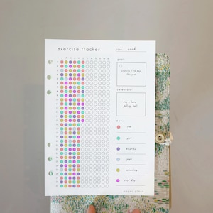 May include: A white exercise tracker sheet with colorful dots for tracking activities. The text "exercise tracker" and "2026" are at the top. The sheet includes a key for different activities and a space to set goals. The words "paper plans" are at the bottom.