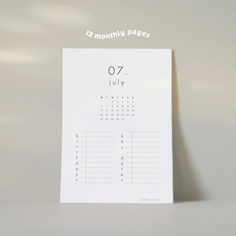 May include: A white paper planner with the month of July displayed. The planner includes a calendar, space for birthdays, and key dates. The text "12 monthly pages" is at the top. The planner is from "paper plans".