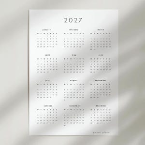 Puede incluir: Un calendario de pared blanco para 2027 con un diseño limpio y minimalista que muestra los doce meses en una cuadrícula. Cada mes incluye el nombre, los días de la semana y las fechas correspondientes en texto negro. Abajo a la derecha dice paper plans.