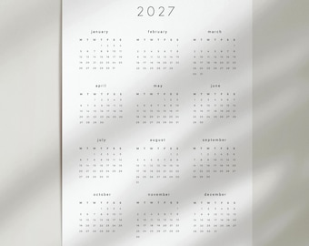 May include: A white 2027 wall calendar featuring a clean, minimalist layout with all twelve months displayed in a grid. Each month includes the name, days of the week, and corresponding dates in black text. The bottom right corner reads paper plans.