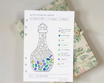 May include: A white paper planner insert titled prioritizing my peace featuring a line art drawing of a bottle filled with various crystal shapes. A color-coded key lists activities like breathe deeply, yoga, and bath with corresponding colored squares.