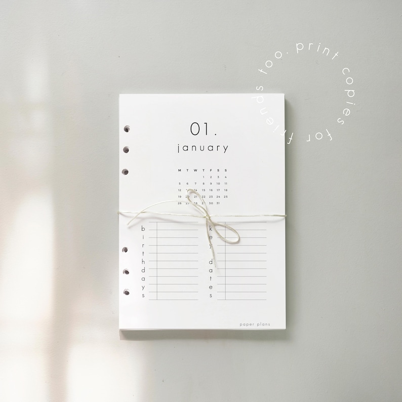 May include: A white paper planner with the date "01. January" printed at the top. The planner includes a calendar, lines for birthdays, and the text "paper plans". It is tied with a string.