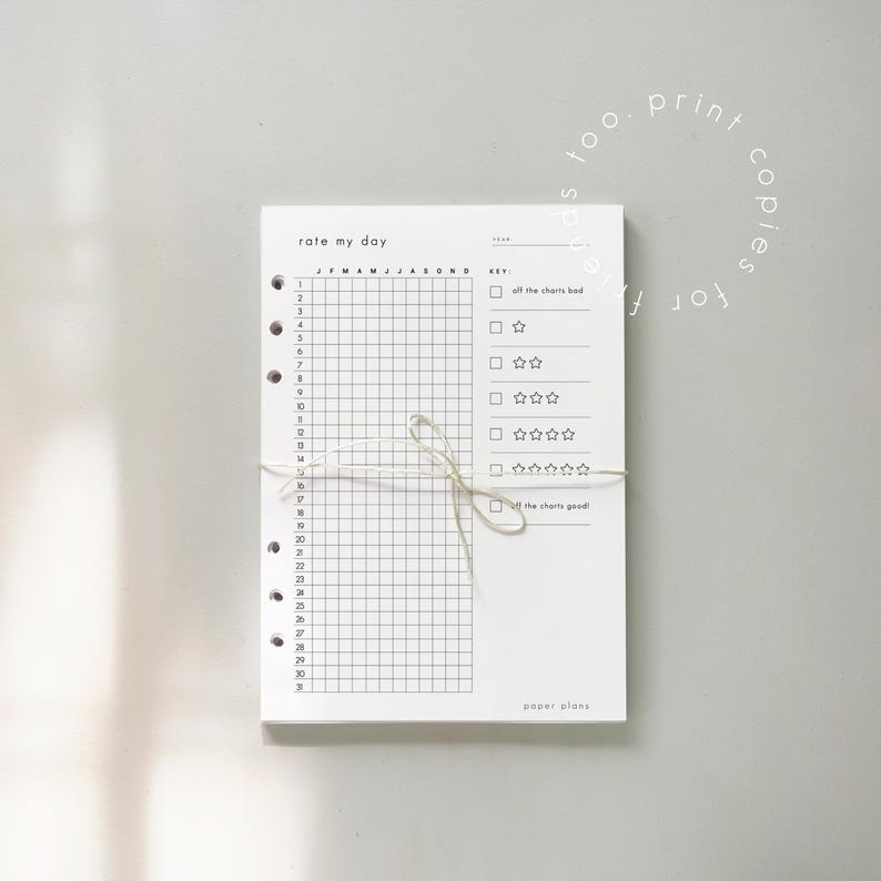 K&ouml;nnte beinhalten: Ein wei&szlig;er Papierplaner mit dem Text "rate my day" oben. Der Planer hat ein Raster zur t&auml;glichen Verfolgung und einen Schl&uuml;ssel zur Bewertung. Er ist mit einer Schnur gebunden und enth&auml;lt den Text "paper plans".