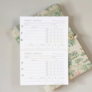 Puede incluir: Hojas de papel blancas para entrenamientos con el texto "today's workout" y secciones para ejercicios, series, cardio y tiempo. Las hojas están sobre un diario con estampado floral y cierre de botón. El texto "paper plans" está en la parte inferior.