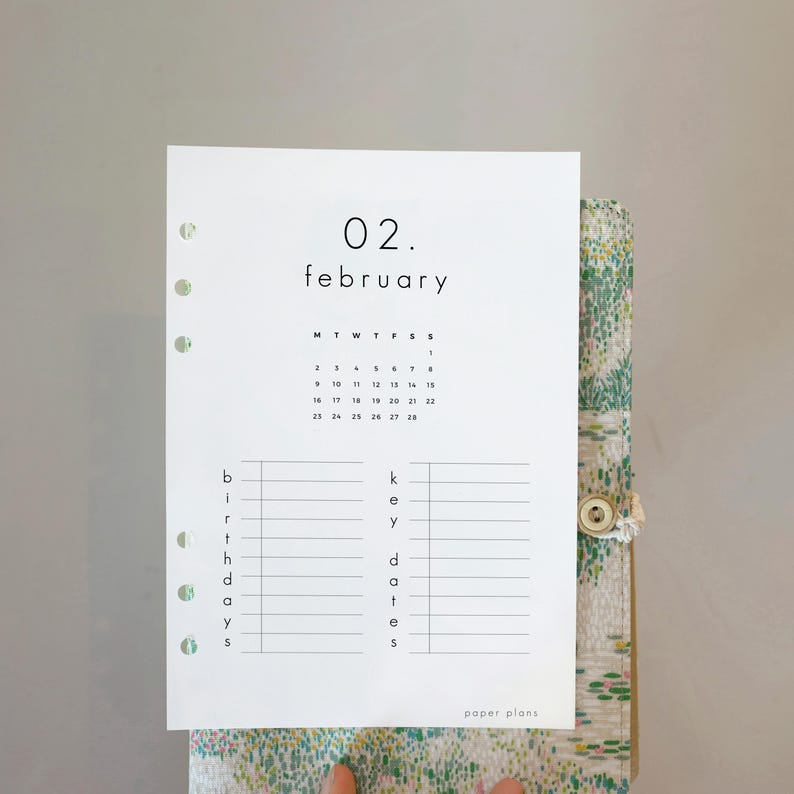May include: A white paper planner insert for February with a minimalist design. The insert features a calendar, the word "february", and sections for birthdays and key dates. The paper is held in a floral patterned binder.