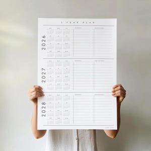 Puede incluir: Un calendario blanco de planificaci&oacute;n de 3 a&ntilde;os con los a&ntilde;os 2026, 2027 y 2028. Cada a&ntilde;o incluye un calendario y espacio para notas personales y profesionales. El texto "3 YEAR PLAN" est&aacute; en la parte superior.