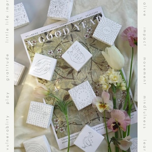 May include: An overhead shot features several small, white square boxes with black line drawings and text, arranged on a floral patterned background. The boxes have words like "Connection" and "Joy". Flowers and the words "A Good Year" are also visible.