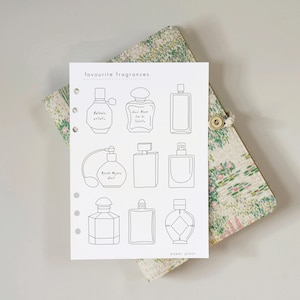 Op de afbeelding: Een witte planner-inlegvel met de kop "favourite fragrances" en de voettekst "paper plans". De pagina bevat negen zwarte lijntekeningen van diverse parfumflesjes, sommige met handgeschreven labels, en is voorzien van vijf ronde perforatiegaten.
