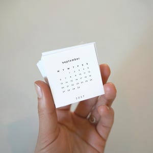 May include: A small, square, white paper calendar page for September 2027. The text reads 'september' at the top, followed by a grid of days of the week labeled M, T, W, T, F, S, S, and the numbers 1 through 30. The year 2027 is printed at the bottom.