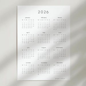 May include: A minimalist 2026 calendar printed on white paper. The calendar features a simple design with the year at the top and months arranged in rows. Each month displays the days of the week and dates. The text "paper plans" is at the bottom.