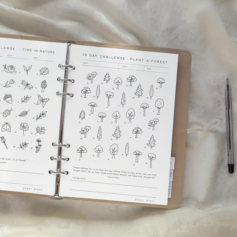 May include: Open planner with a 30-day challenge to plant a forest, featuring tree illustrations. The planner is open to a page with a nature theme, including drawings of insects and plants. A pen rests on the right side.