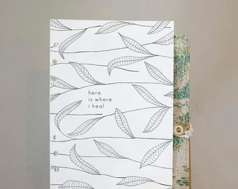 May include: A white rectangular planner insert featuring a black line-art pattern of leaves on stems. The text "here is where i heal" is printed in the center, with "paper plans" at the bottom right. The page has six circular binder holes.