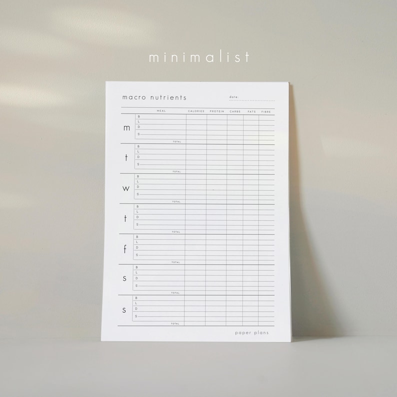 May include: A white paper planner with the words "macro nutrients" at the top. The planner has columns for meal, calories, protein, carbs, fats, and fiber. The word "minimalist" is at the top, and "paper plans" is at the bottom.