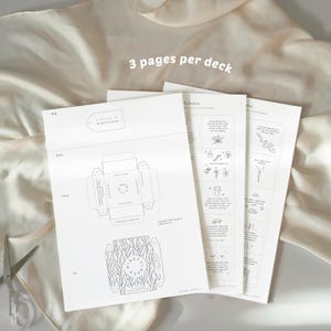 May include: Three white paper sheets with black line drawings and text, including a box template and mindfulness prompts. The text "3 pages per deck" is at the top. A pair of scissors is in the lower left corner.