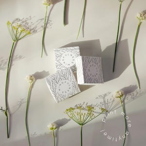 May include: Three white boxes with a black tree branch design and the word "MINDFULNESS" in a circle. The boxes are surrounded by white flowers and green stems on a white background. The words "print more anytime!" are in a circle.